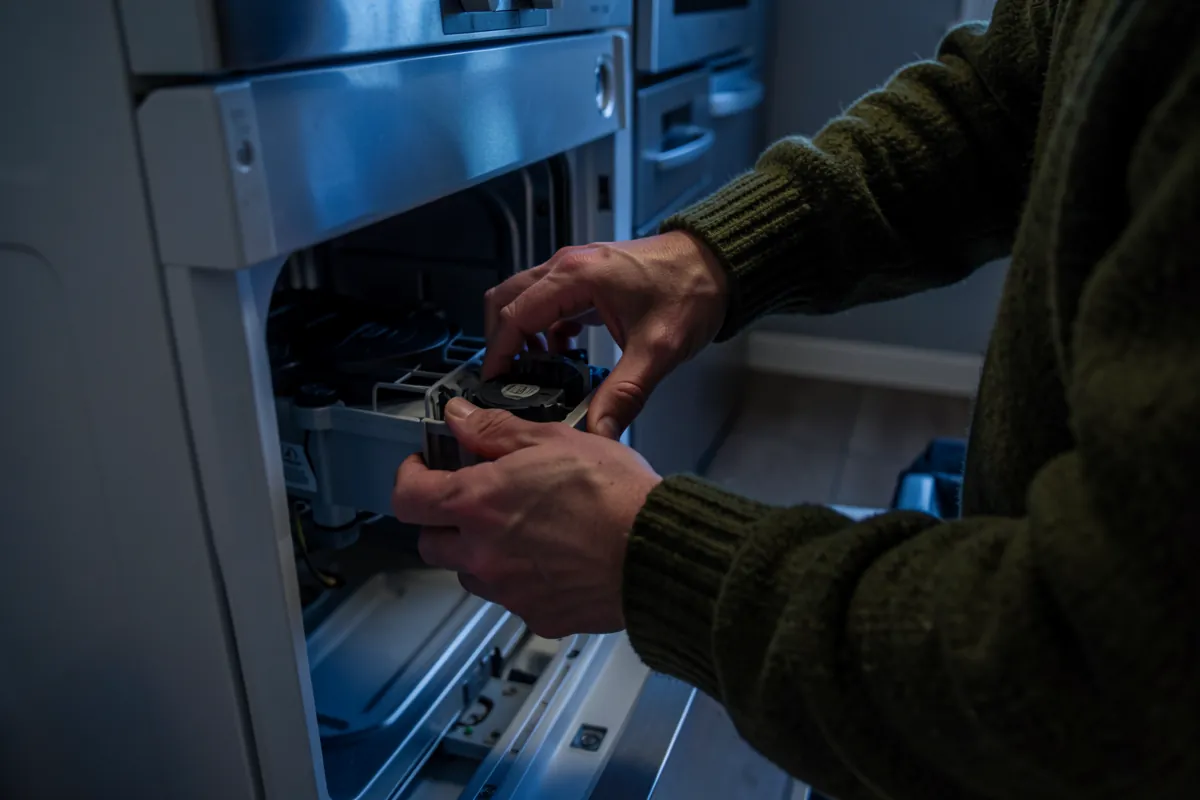 Henkilö tarkistaa astianpesukoneen sisäosia veden lämpenemisongelmien selvittämiseksi.