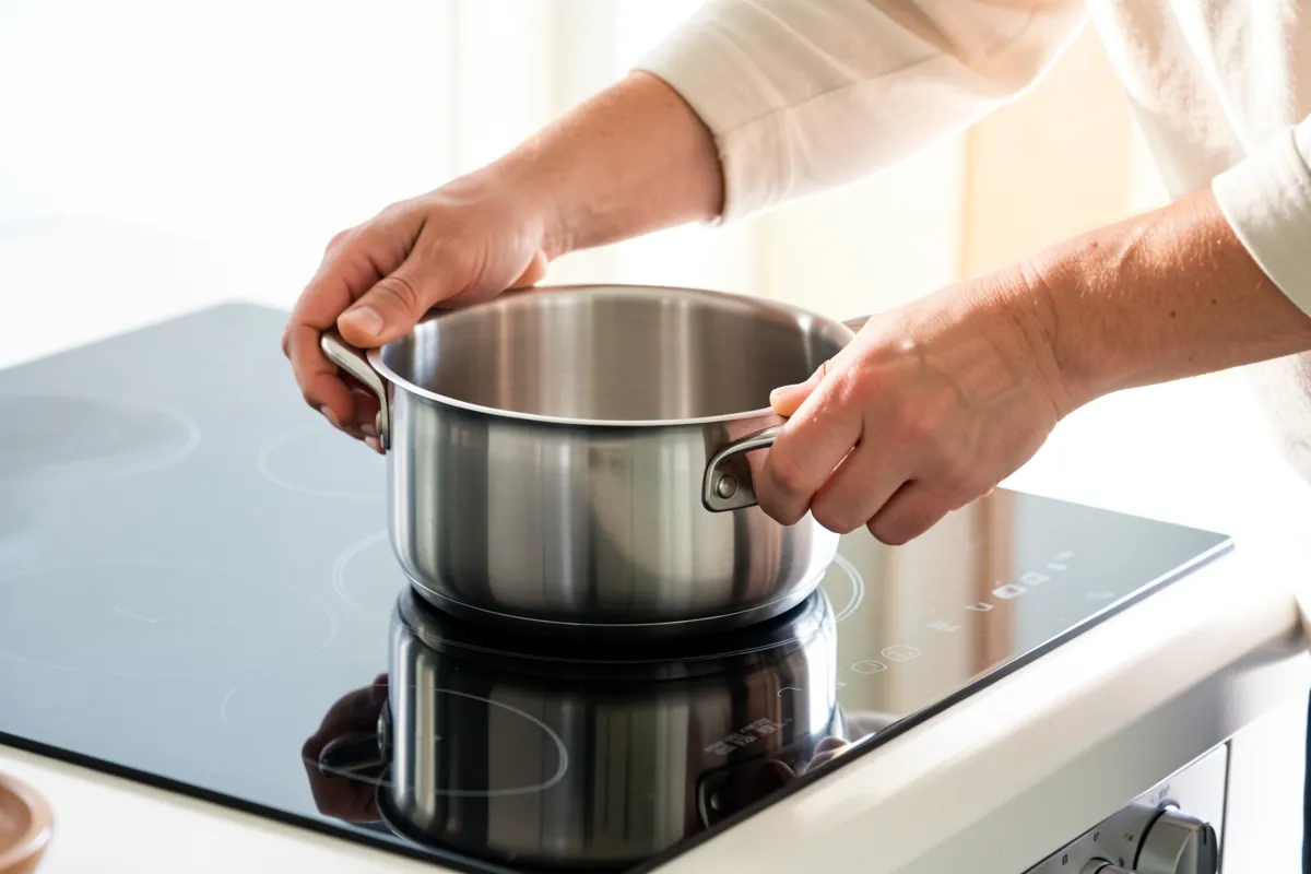 Kädet asettamassa teräskattilaa induktioliedelle vianmäärityksen aikana.